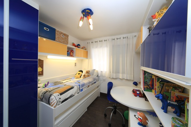 vista do quarto infantil a partir da porta, após a reforma, com a cama com cama inferior junto à árede esquerda e os armários com mesa de estudos arredondada à direita.