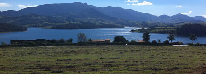 Vista a partir do terreno em Piracaia com vegetação rasteira em toda a área e a represa ao fundo.