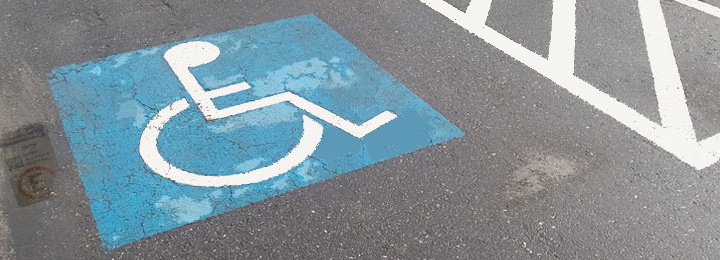 Vaga reservada para PcD em piso de asfalto, com o Símbolo Internacional de Acesso aplicado no centro e área de proteção de estacionamento ao lado, na cor branca.