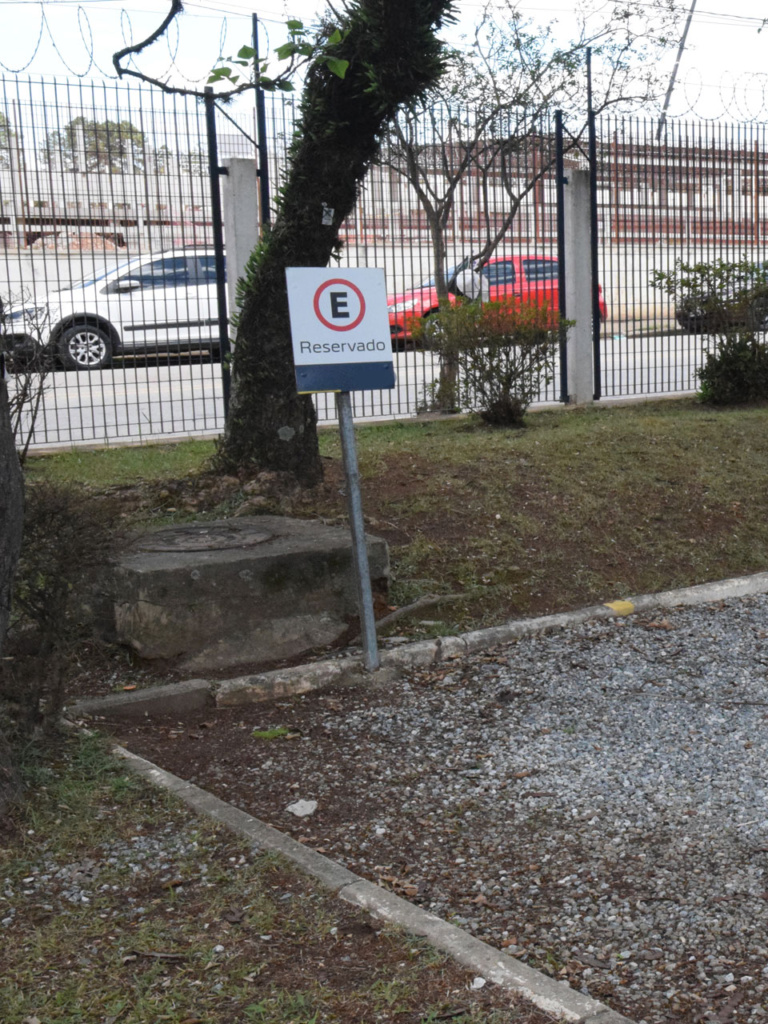 Vaga reservada para pessoa com deficiência instalada de forma errada em piso de pedriscos e com a placa de sinalização fora dos padrões.